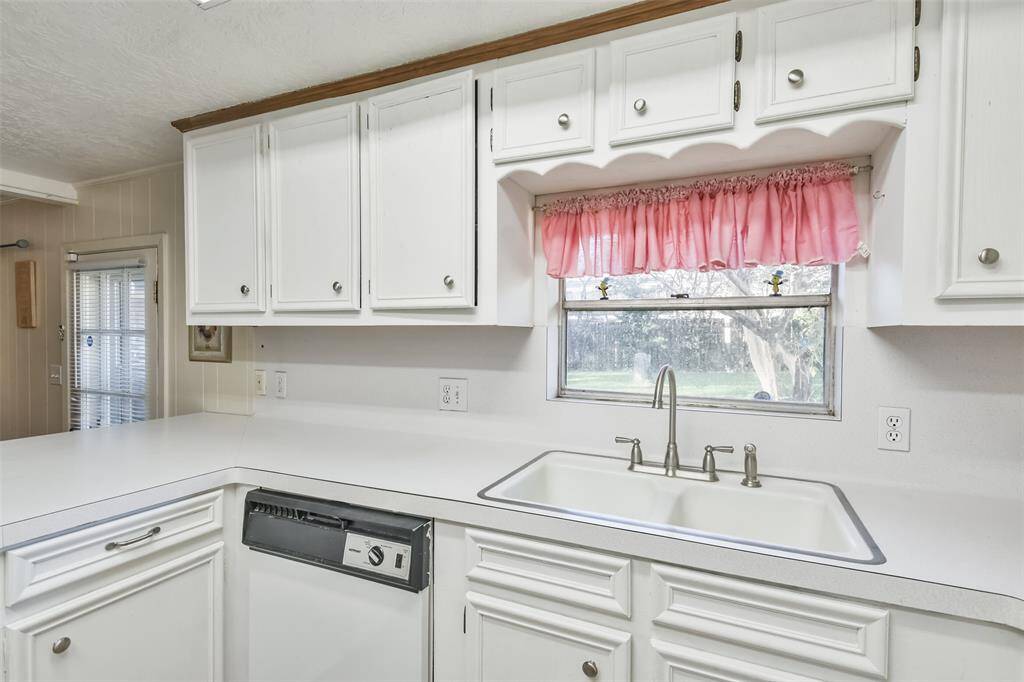 Charming kitchen sink area featuring white cabinetry, a stainless steel faucet, and a large window offering views of the backyard. The built-in dishwasher ensures convenience, while the expansive counter space enhances functionality