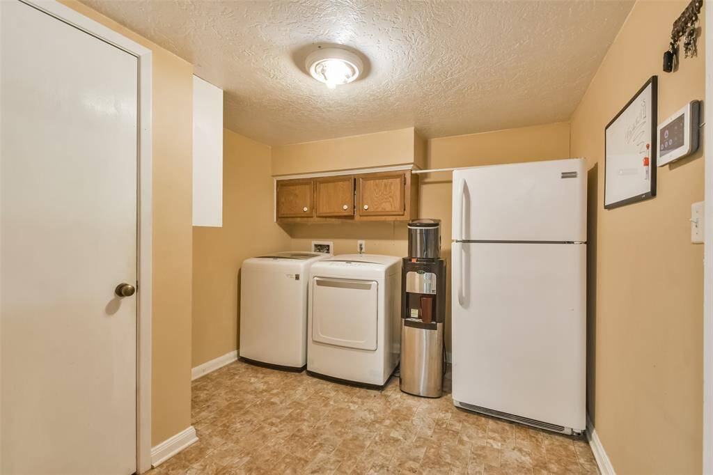 Functional laundry room featuring a washer, dryer, and additional storage with upper cabinets. The space is enhanced by a refrigerator, water dispenser, and easy-to-clean flooring, offering practicality and convenience