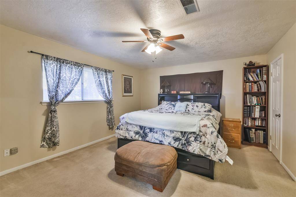 Spacious primary bedroom featuring soft carpet flooring, a ceiling fan, and a large window with patterned curtains for natural light