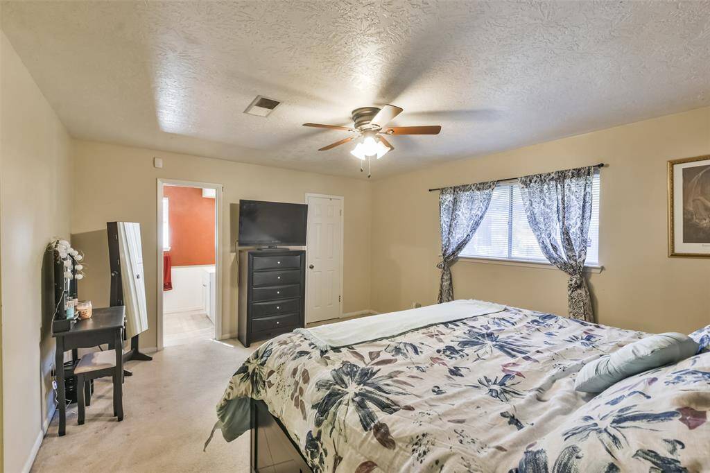 Primary bedroom with a spacious layout, a ceiling fan, soft carpeting and large windows with patterned curtains for natural light. An en-suite bathroom adds convenience and privacy.