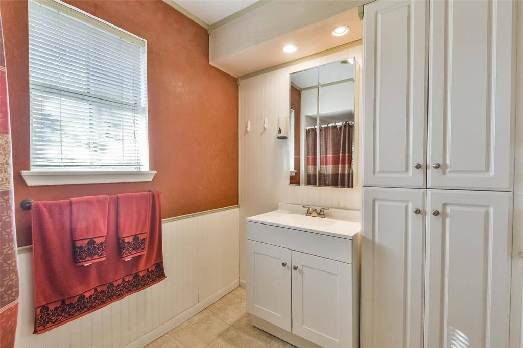 Warm and inviting primary bathroom featuring terracotta walls with beadboard wainscoting, a sleek white vanity, and ample built-in cabinetry for storage. A well-placed window provides natural light, complemented by recessed lighting for a bright and functional space