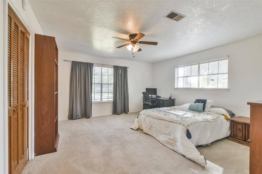 Spacious third bedroom offering plenty of room for versatility, featuring soft carpet flooring, large windows that fill the space with natural light, and a ceiling fan for comfort. The expansive layout easily accommodates a bed, desk, and additional furniture, highlighting the generous size of the home’s bedrooms