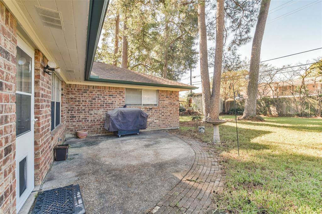Charming backyard featuring a brick patio area perfect for outdoor grilling and relaxation. Surrounded by mature trees and lush greenery, this space offers a peaceful retreat with plenty of room for gardening or entertaining