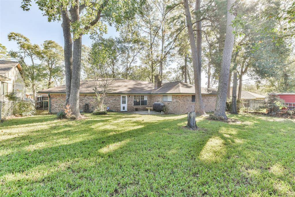 Expansive backyard with a lush green lawn shaded by mature trees, offering ample space for outdoor activities or relaxation. The brick exterior of the home adds charm, while the patio area provides a great spot for grilling and entertaining.