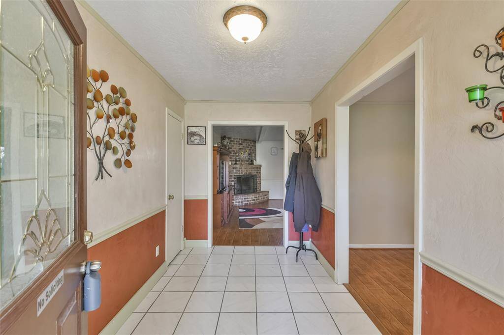 Welcoming entryway featuring a combination of tiled flooring and warm two-tone walls, leading to a cozy living room with a brick fireplace. Decorative accents add character to the space