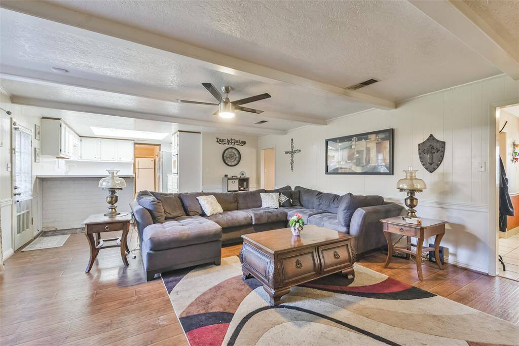 Open-concept living room with a seamless flow to the kitchen, featuring a spacious sectional sofa, wood-look flooring, and a colorful area rug. The ceiling fan and abundant natural light add to the room’s comfort, while the white brick breakfast bar provides charm and functionality