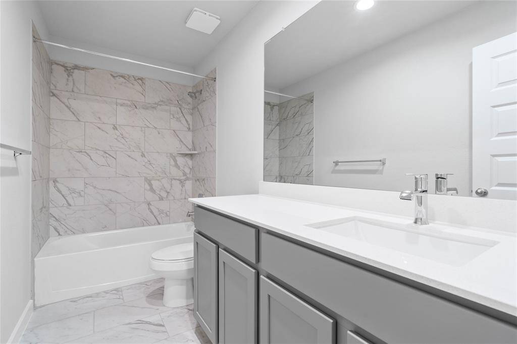 Secondary bath features tile flooring, bath/shower combo with tile surround, stained wood cabinets, beautiful light countertop, mirror, dark, sleek fixtures and modern finishes!