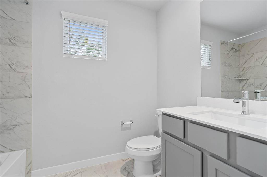 Secondary bath features tile flooring, bath/shower combo with tile surround, stained wood cabinets, beautiful light countertop, mirror, dark, sleek fixtures and modern finishes!