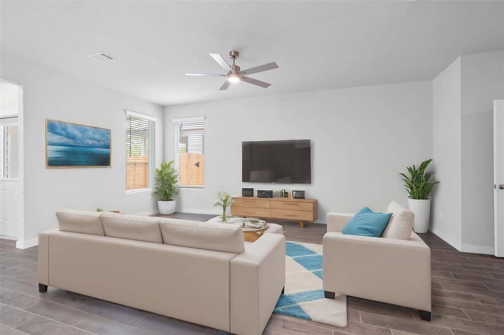 This family room is a perfect room! Featuring custom paint, high ceilings with ceiling fan, wood look tile flooring, and windows providing natural light into this beautiful room.
