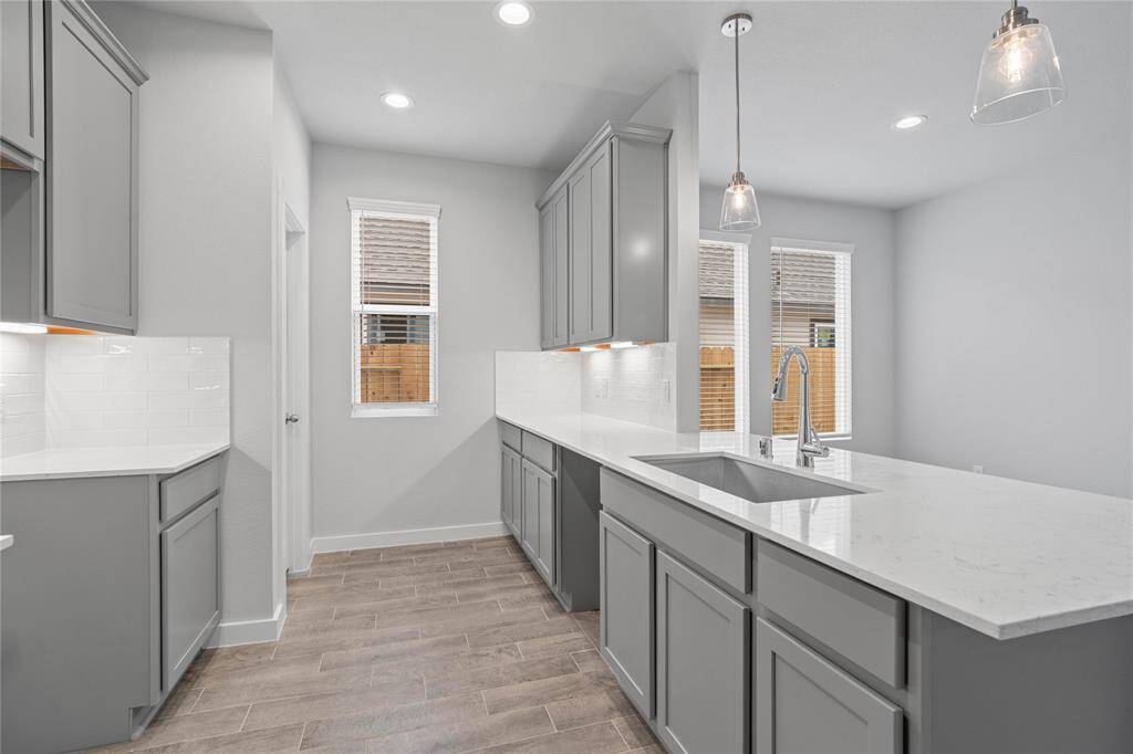 Additional view of this gorgeous kitchen showcases the quartz countertops, stainless steel single single sink, pendant lighting and the beautiful cabinetry that provides plenty of storage space.