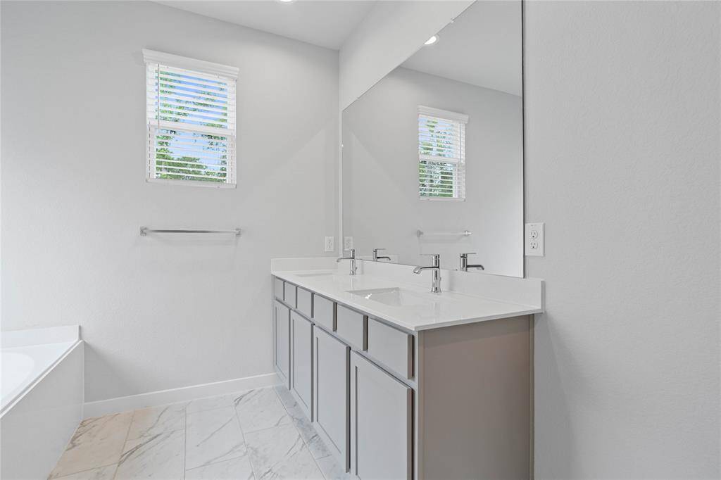 Wow! Look at this primary bathroom! Complete with stained cabinets and sleek light countertops, dual vanities, large modern tile flooring, and a window allowing in the natural light.