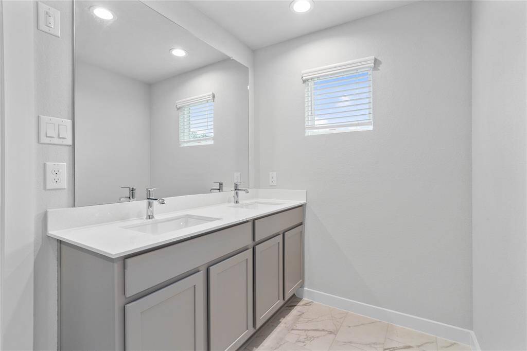 Wow! Look at this primary bathroom! Complete with stained cabinets and sleek light countertops, dual vanities, large mirror, tile flooring, and a window allowing in natural light!