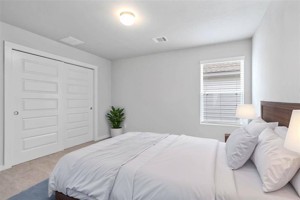This secondary bedroom features high ceilings, light, custom paint, plush carpet, ample closet space, and a large window.