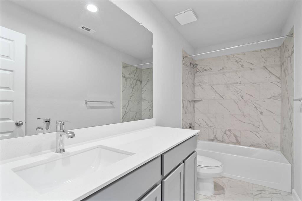 Secondary bath features tile flooring, bath/shower combo with tile surround, stained wood cabinets, beautiful light countertop, mirror, sleek fixtures and modern finishes!