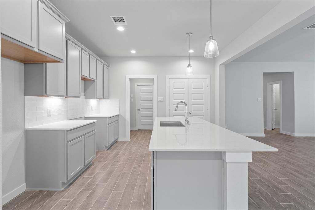 Additional view of this gorgeous kitchen highlighting the gorgeous kitchen island with single bowl sink and quartz countertop, under cabinet and pendant lighting, and the pantry!