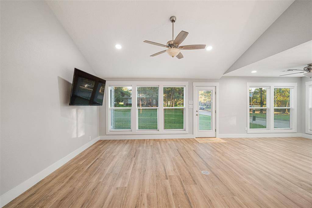 This spacious living area features large windows and a glass door that provide abundant natural light, elegant wood flooring, and a ceiling fan for comfort. Ideal for relaxation and entertaining.