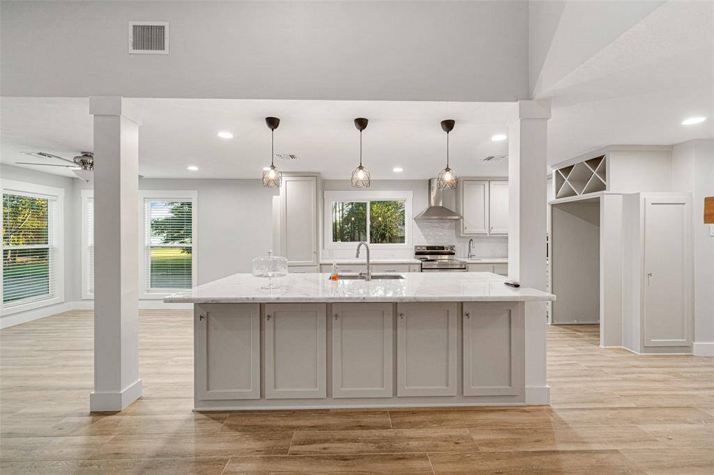 This photo showcases a modern, open-concept kitchen with a large island, pendant lighting, and stainless steel appliances. It features light-colored cabinetry and wood-look flooring, providing a bright and inviting atmosphere. The kitchen opens to a spacious living area with large windows, enhancing natural light.