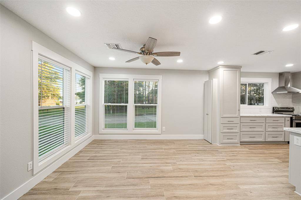 Bright and spacious open-plan area with large windows, modern light fixtures, and wood-look flooring. The kitchen features sleek cabinets, stainless steel appliances, and a ceiling fan enhances comfort. Perfect for modern living.