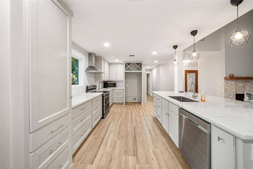 This modern kitchen features sleek white cabinetry, stainless steel appliances, and a spacious island with pendant lighting. The open layout and wood-style flooring create a warm and inviting atmosphere, perfect for entertaining.