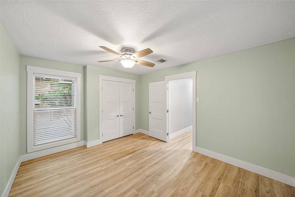This room features light green walls, a ceiling fan, and wood-style flooring. It includes a window with blinds and a double-door closet, creating a bright and airy space.