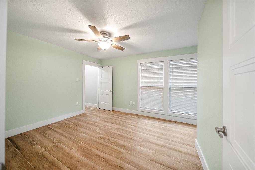 This room features light green walls and wood-look flooring, creating a cozy atmosphere. It includes a ceiling fan for comfort and two large windows for natural light.