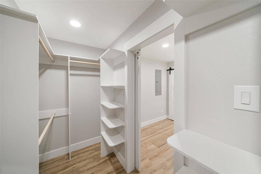 This photo showcases a spacious walk-in closet featuring built-in shelves, hanging rods, and a modern wood floor. Bright overhead lighting enhances the clean, neutral color palette.