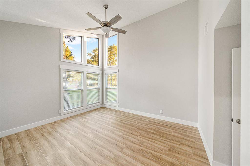 Bright, spacious room with high ceilings and large windows, featuring elegant wood flooring and a modern ceiling fan. Perfect for natural light and an open feel.