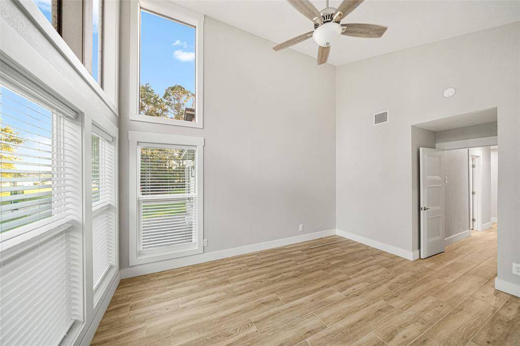 Bright and spacious room with high ceilings, large windows for natural light, wooden flooring, and a ceiling fan. Ideal for a modern, airy feel.