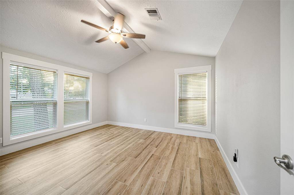 This bright room features large windows with blinds, a ceiling fan, and wood-look flooring, offering a modern and airy feel.