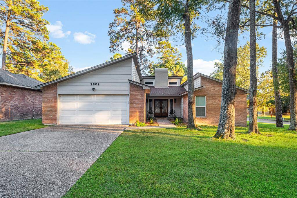 Charming single-story home with a modern exterior featuring brick and wood accents. It includes a two-car garage and a welcoming front porch. The property is surrounded by mature trees, offering ample shade and a spacious front lawn.