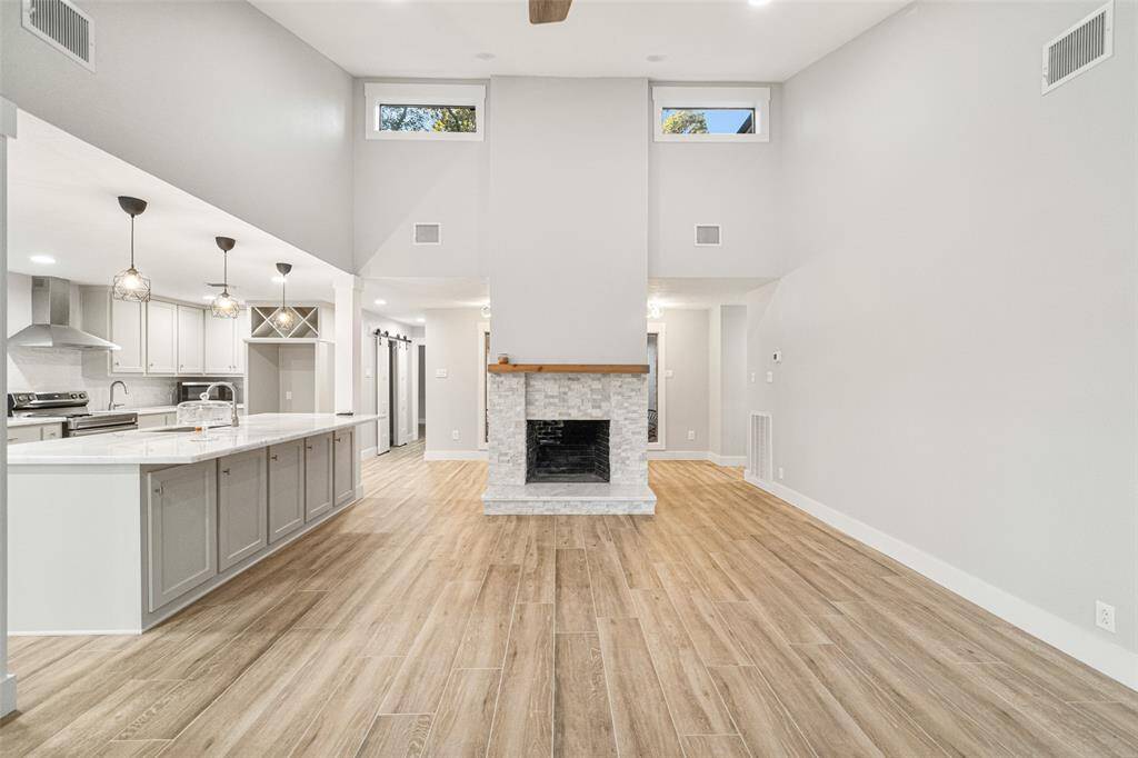 This spacious open-concept living area features high ceilings, a modern kitchen with an island, and a cozy fireplace. The light wood flooring and neutral palette create a bright, inviting atmosphere.