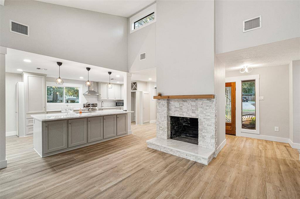This open-concept living area features a modern kitchen with a large island, elegant pendant lighting, and a cozy fireplace. The space is enhanced by high ceilings and natural light, creating a warm and inviting atmosphere.
