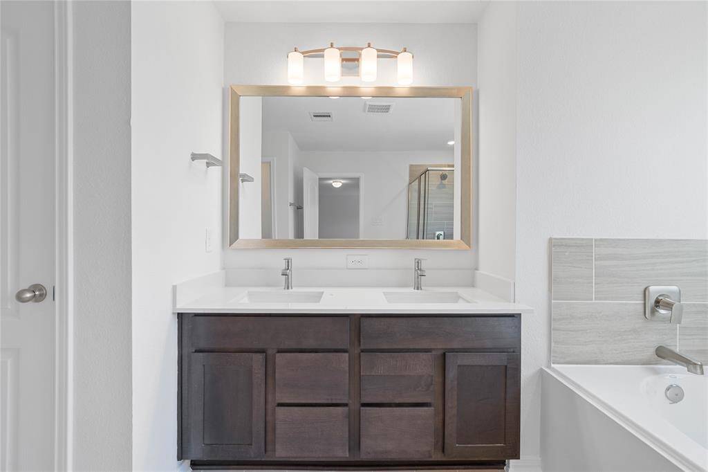 This primary bathroom is definitely move-in ready! Featuring stained cabinets with light countertops, dual vanities, framed mirror, high ceilings, neutral paint, sleek and modern finishes.