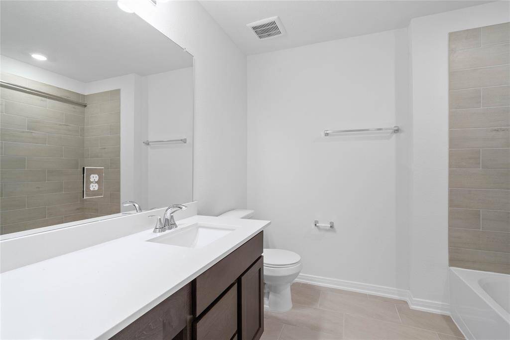 Secondary bath features tile flooring, bath/shower combo with tile surround, stained wood cabinets, beautiful light countertops, mirror, sleek fixtures and modern finishes.
