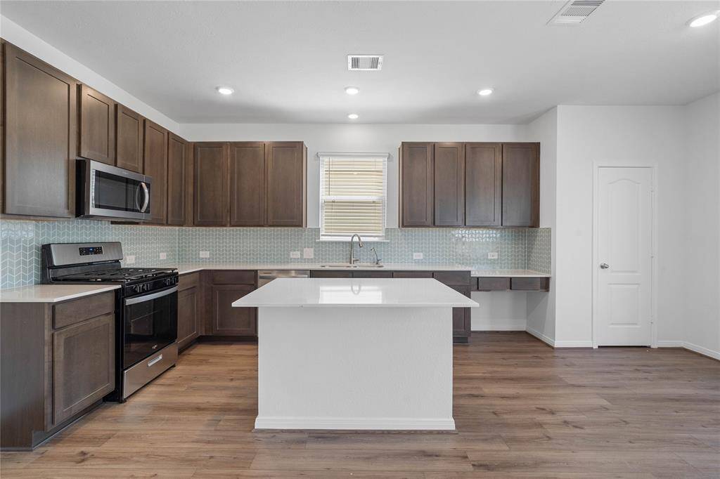 Another view of this spacious kitchen featuring high ceilings, stained wood cabinets, granite countertops, SS appliances, modern tile backsplash, recessed lighting, large kitchen island with space for a breakfast bar, and a pantry all overlooking your huge family room.