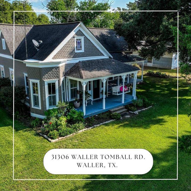 This is an aerial view of this charming single-family home featuring a gray exterior with white trim, a large covered front porch, and a neatly maintained lawn. The home is located at 31306 Waller Tomball Rd., Waller, TX.