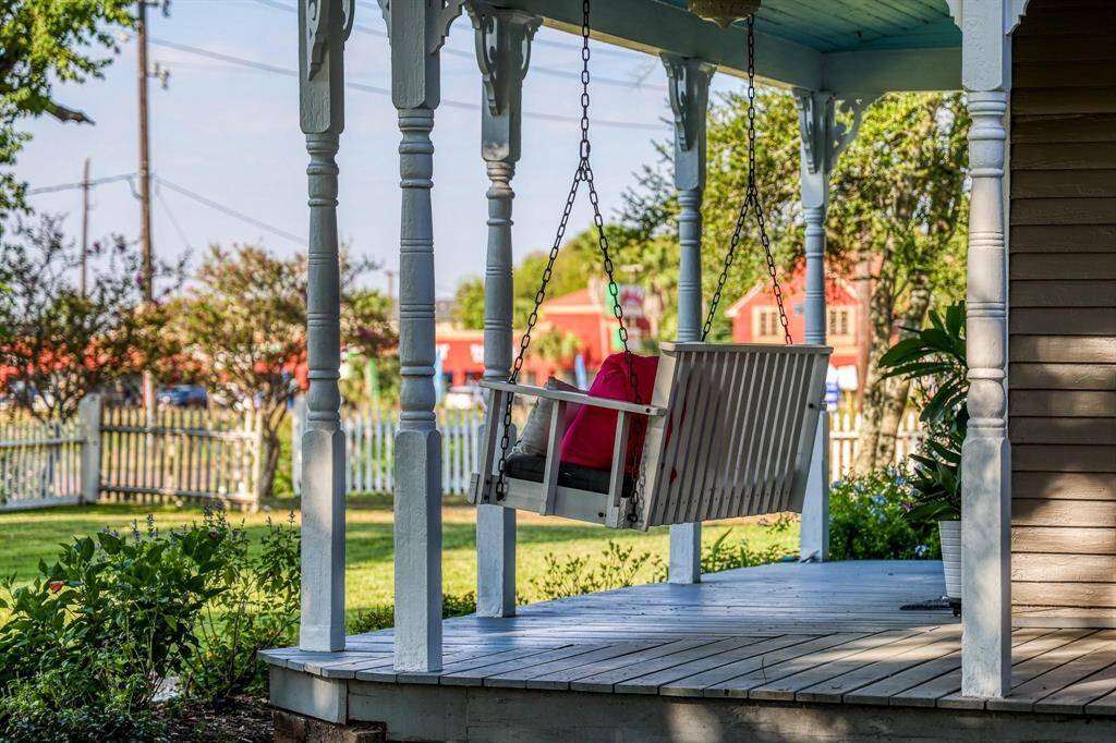 This image showcases a charming porch with traditional white columns and a cozy swing, offering a peaceful spot to relax and enjoy the view of the surrounding greenery and neighborhood.