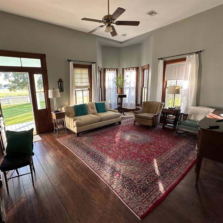This is a spacious living room featuring hardwood floors, elegant wood trim around doorways, a high 11.5 foot ceilings with a fan, and a cozy seating area.