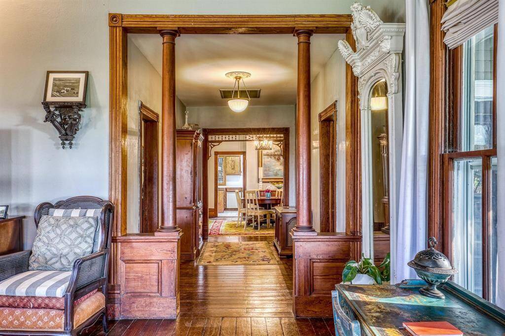 This photo showcases the classic hallway with rich wooden architectural details, including columns and trim, leading to a dining area. The space features hardwood floors, an elegant light fixture, and large windows allowing for ample natural light.