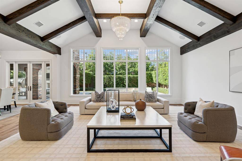 [Family Room] A bright and inviting living area boasting soaring vaulted ceilings with exposed wooden beams, 2 stunning chandeliers, and expansive windows that overlook the beautiful pool.