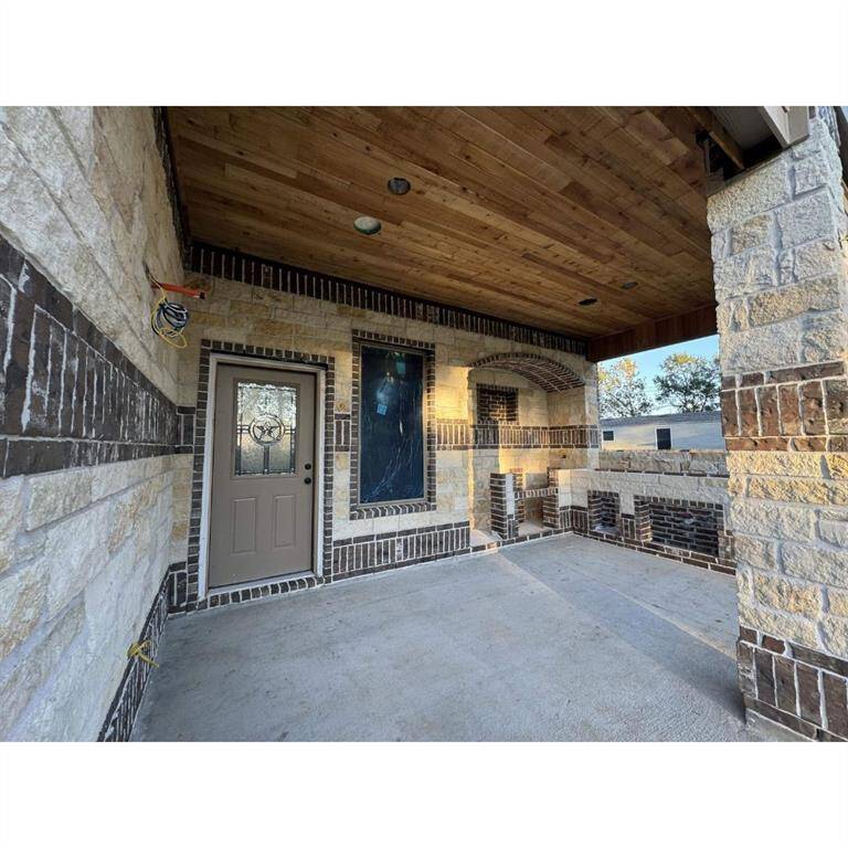 Covered porch with a wood ceiling and brick and stone walls. It features a decorative front door with a glass insert, providing a welcoming entryway.