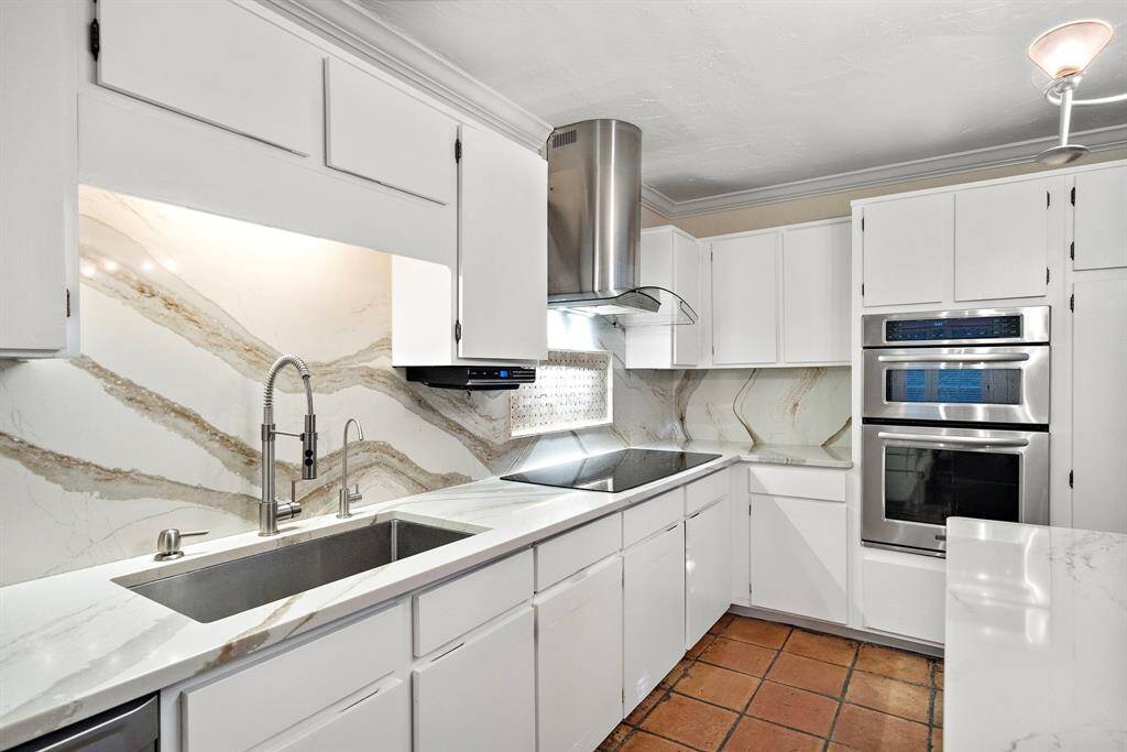 The upgraded kitchen showcases expansive counters, sleek double ovens, a stylish vent hood, and a deep stainless steel sink, adding both practicality and elegance.