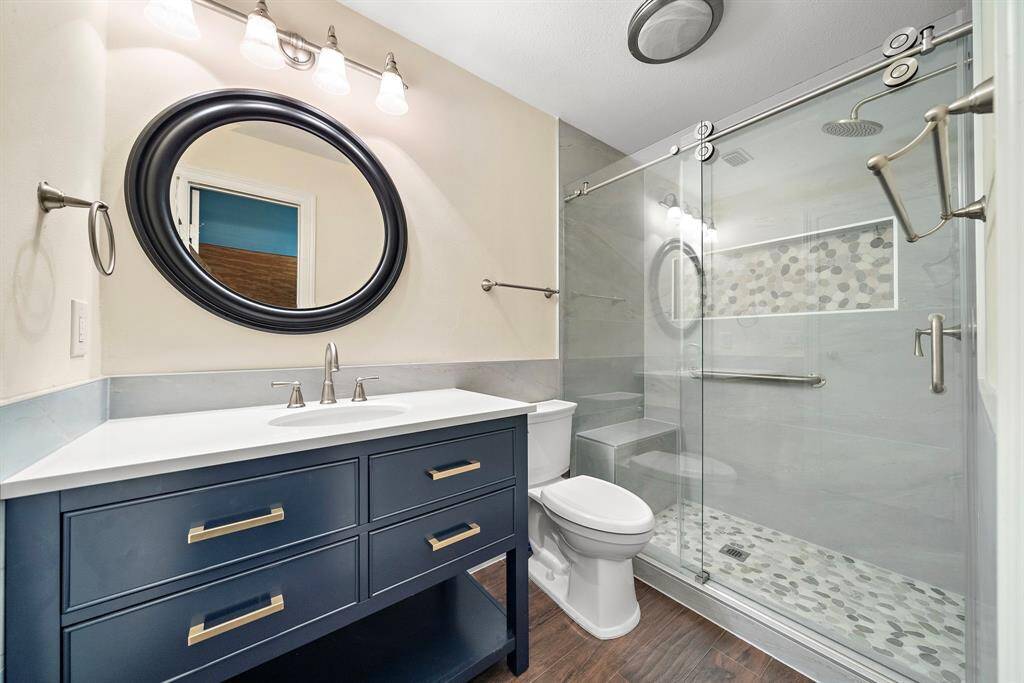 Sleek design meets functionality in the updated secondary ensuite bath, with a modern navy vanity and a glass-enclosed shower featuring a bench and intricate tilework.