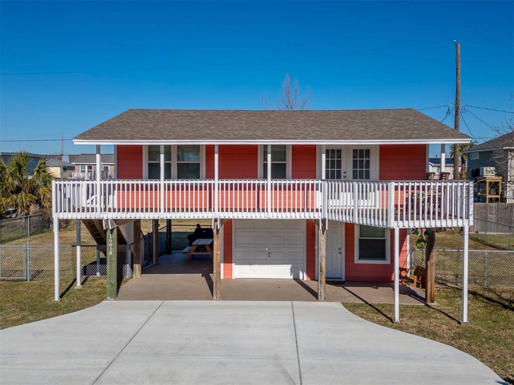 This elevated home features a vibrant exterior with a spacious balcony, a large driveway, and a covered area underneath perfect for parking or outdoor activities. Ideal for coastal living.
