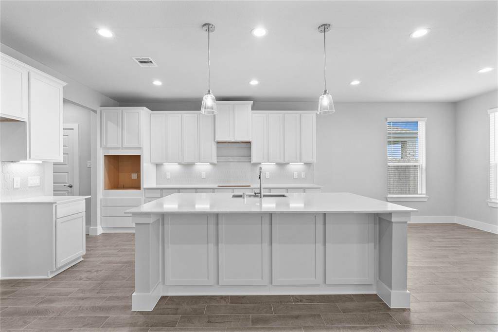 Another view of this spacious kitchen highlighting the beautiful cabinetry, kitchen island with pendant lighting, space for stainless steel appliances, including the cooktop stove and oven.