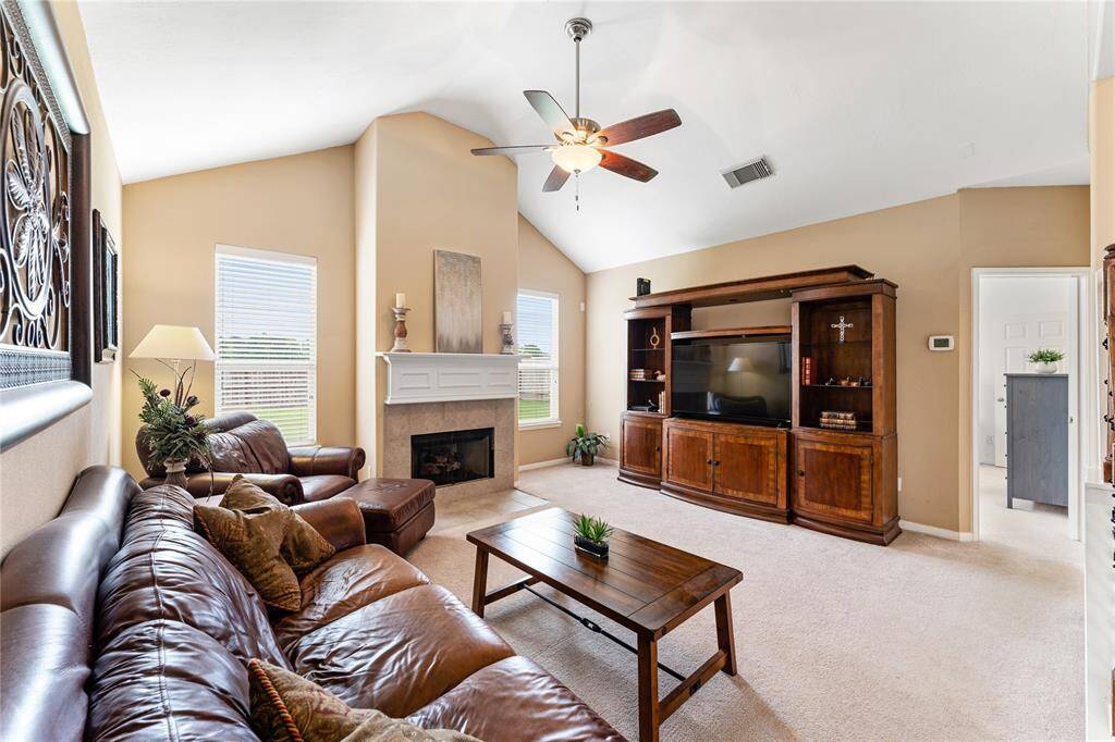 This inviting living room features high ceilings, celing fan. The open layout seamlessly connects to the kitchen, which has a breakfast bar. A staircase with wrought iron railing adds a touch of sophistication.