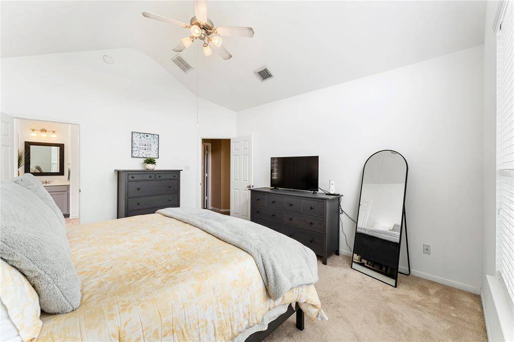 Spacious primary suite has a ceiling fan, plush carpet and peeks into your private bathroom.