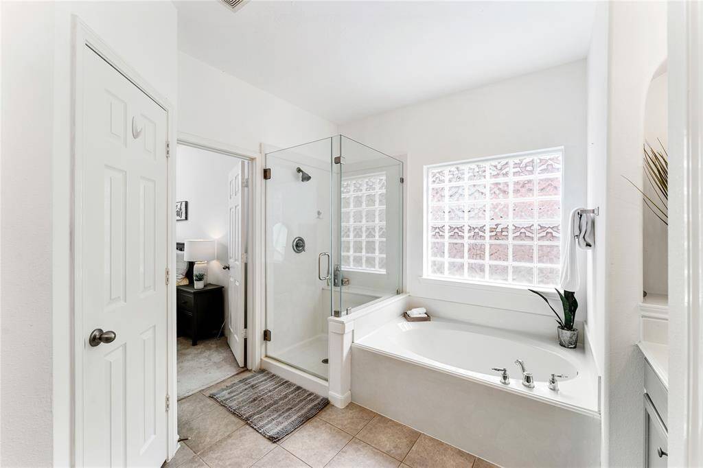 Bright and spacious bathroom featuring a large glass-enclosed shower, a soaking tub, dual vanities with blue cabinetry, and a large window for natural light.