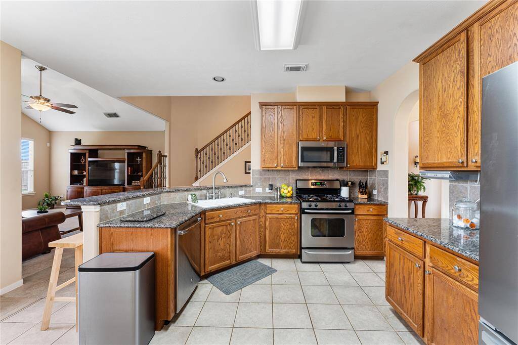 This bright kitchen features stainless steel appliances, granite countertops, and wooden cabinetry. It opens to a cozy breakfast area with large windows, offering ample natural light and a view into the living room with a fireplace.