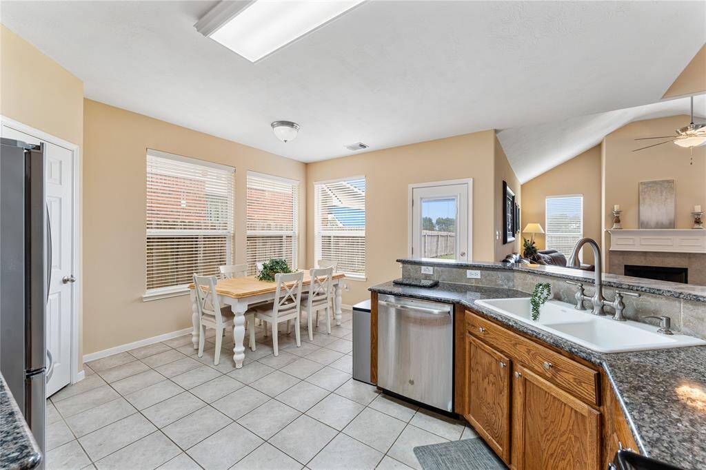 This photo showcases a spacious kitchen with oak wooden cabinets, stainless steel appliances, and granite countertops. Breakfast bar, tile flooring, and opens into a cozy living area.